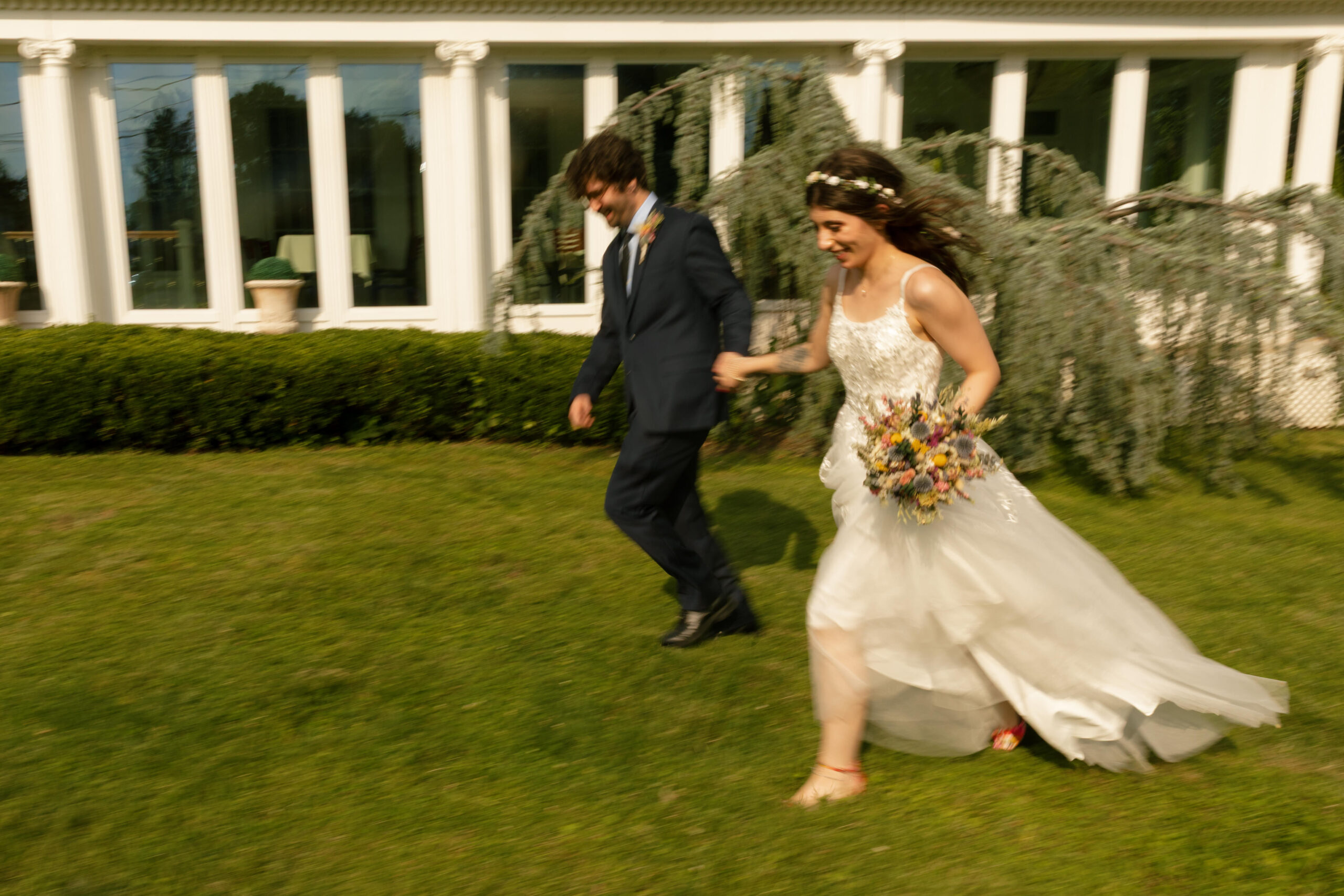Bride and groom running joyfully in front of the Bella Tori mansion in Langhorne, PA