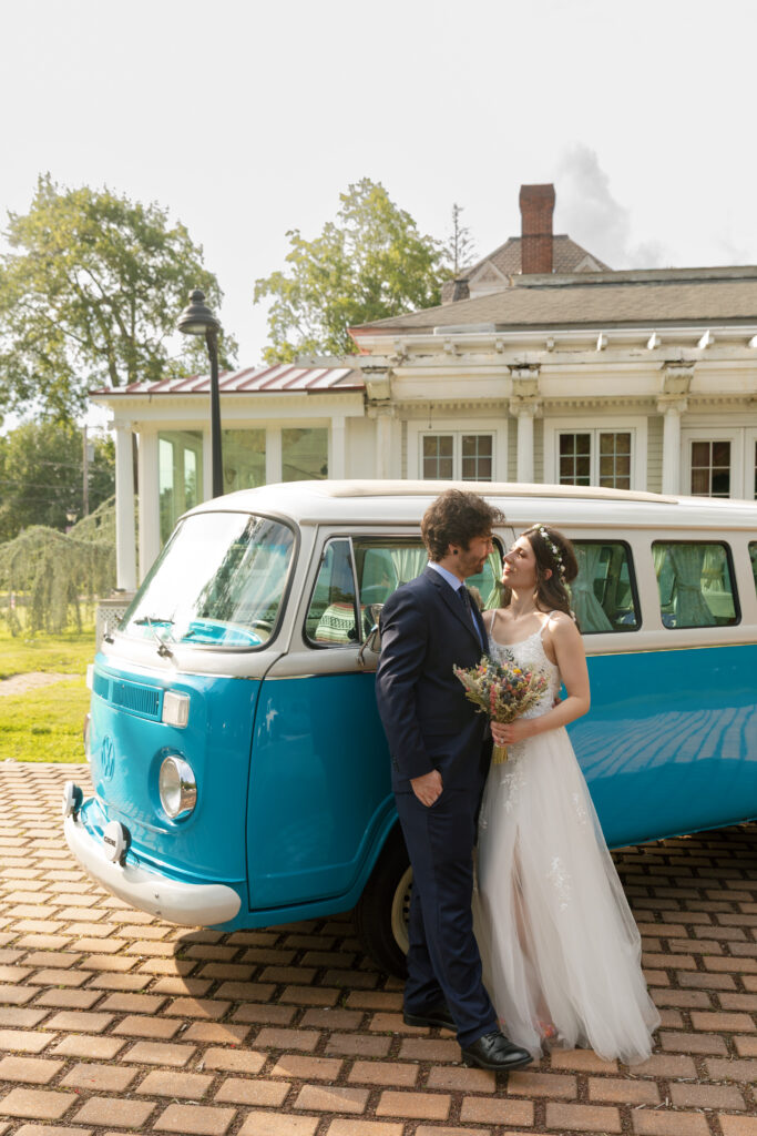 Rachel and Jake pose with a baby blue vintage Volkswagen at their Bella Tori at the Mansion wedding