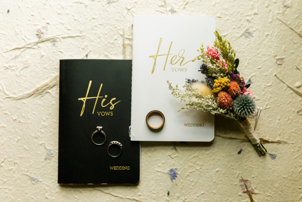 Handwritten vow books resting on a vintage table with pink florals and wedding rings